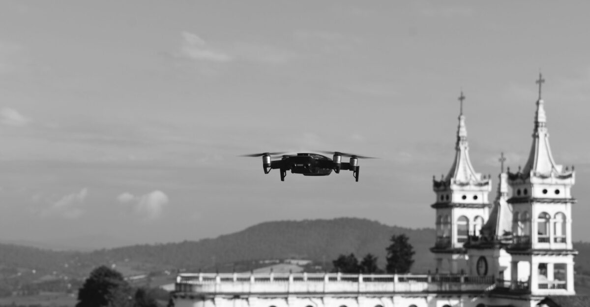 grayscale photo of black plane flying over white building