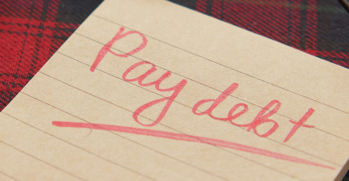 a note that says pay debt next to a pen and glasses