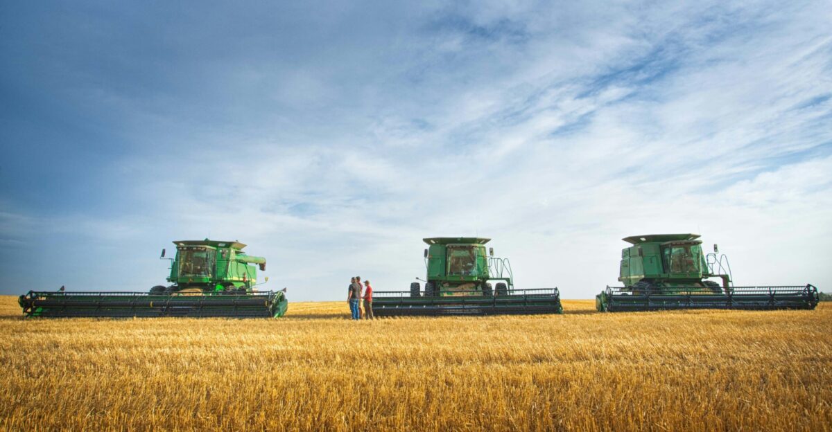 a couple of people standing in a field next to a couple of large green farm
