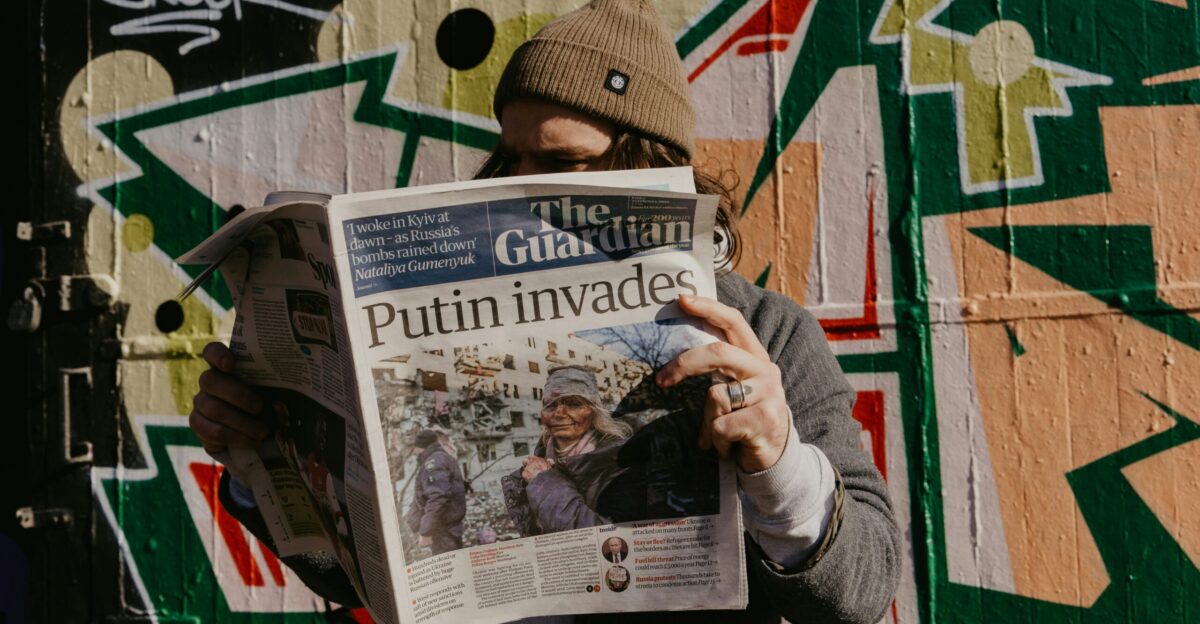 a man reading a newspaper in front of a graffiti covered wall