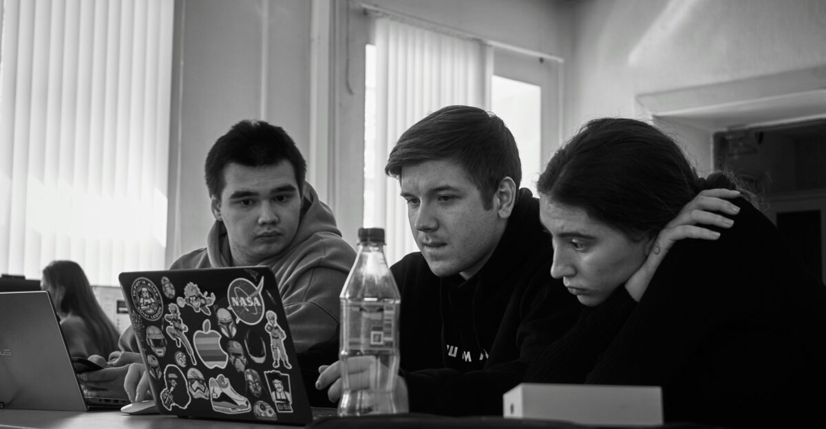 three people sitting at a table looking at a laptop