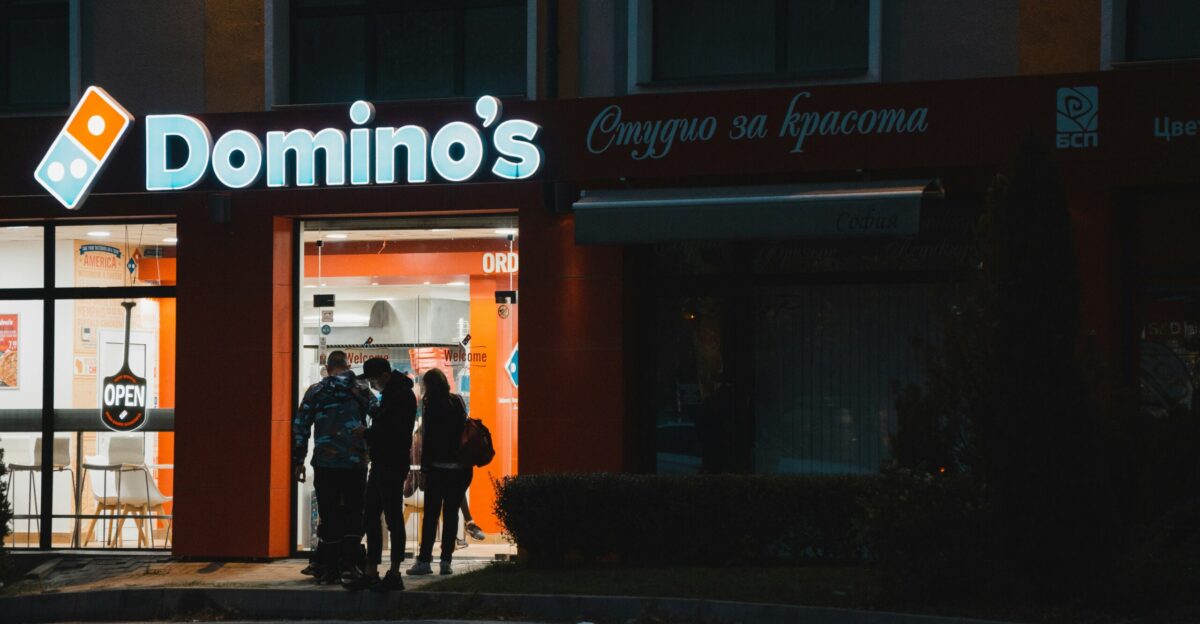 a group of people standing outside of a domino s store