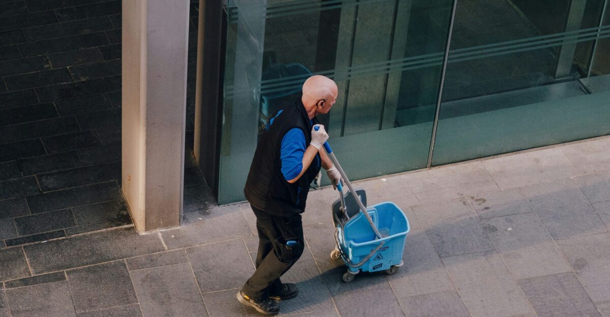 A man pulls a cleaning cart near a building