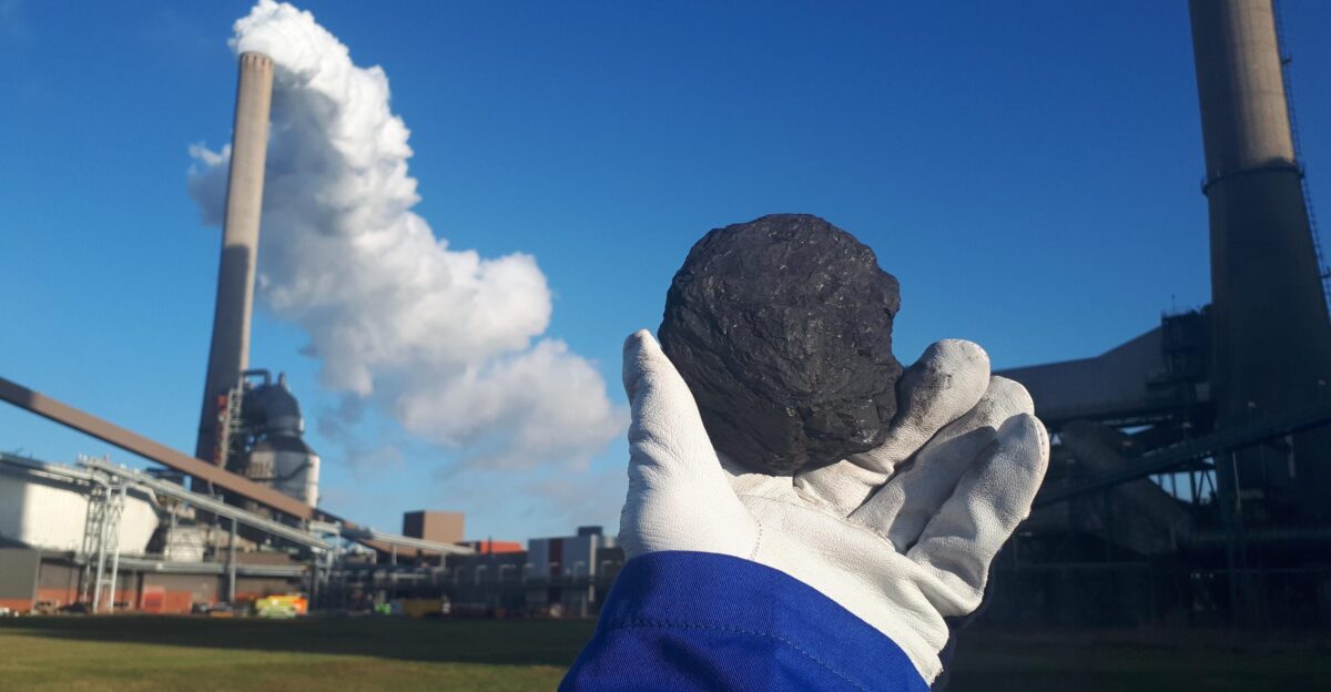 Worker holding up a piece of coal in front of a coal firing power plant in the Netherlands