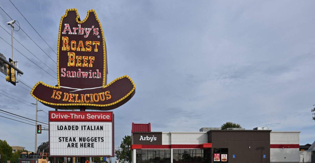 The classic Arby s sign that is in the shape of a hat and says Arby s Roast Beef Sandwich Is Delicious with the restaurant in the background and the parking lot and sign in the foreground 2918 East Eleventh Street Tulsa Oklahoma 74104
