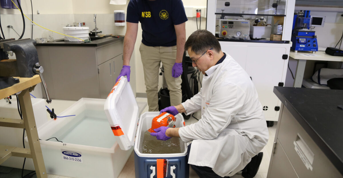 In this photo taken on March 2 2019 NTSB engineers Sean Payne center and Joe Gregor removing cockpit voice recorder from cooler used to transport from accident scene of the Feb 23 cargo jet that crashed in Trinity Bay in Anahuac TX NTSB photo taken by Keith Holloway