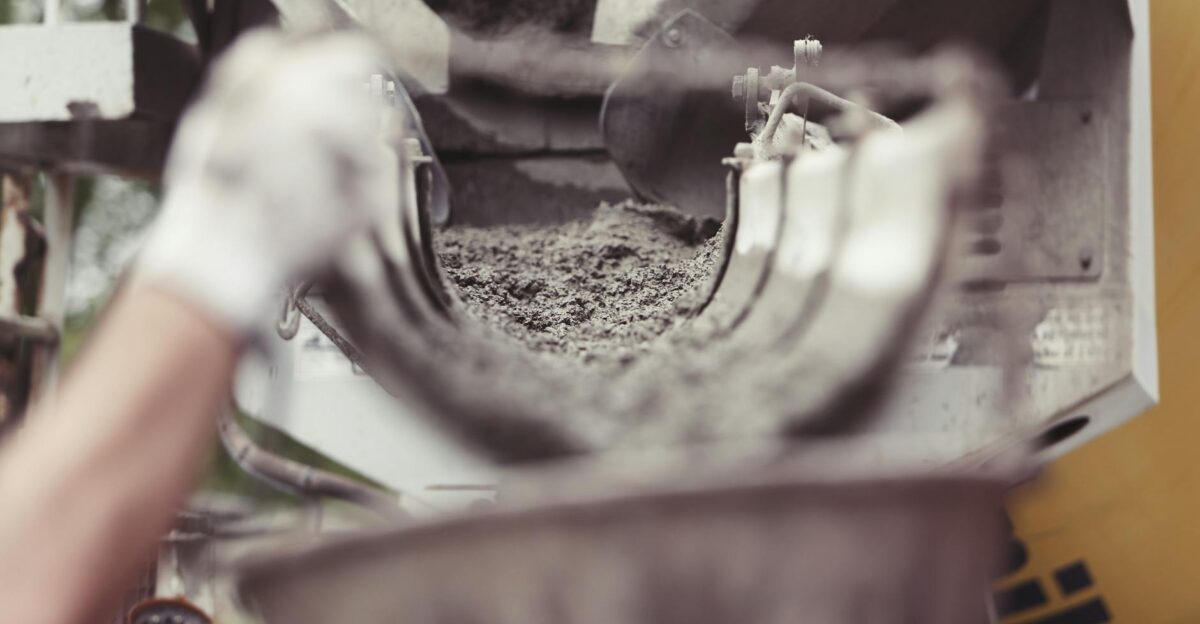 Close-up of concrete being poured from a mixer truck at a construction site with a worker s hand visible