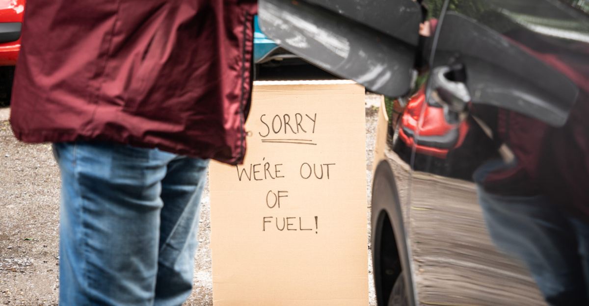 Photograph of a person standing next to a car with the fuel cap open.  There is a sign in the background reading "Sorry, We're out of Fuel!"
This image is free to use on the condition that a link to <a rel="nofollow" class="external free" href="https://www.icompario.com/nl-be/">https://www.icompario.com/nl-be/</a> is included as attribution.