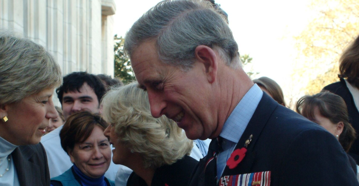 Group of figures outdoors; in the foreground, Karen Hastie Williams and Charles, Prince of Wales, shake hands.
