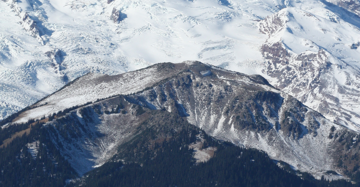 Mount Rainier with its main summit Columbia Crest 14410 feet left Liberty Cap 14112 feet is to the right behind Russell Cliff Curtis Ridge descends to the right from Russell Cliff Massive Emmons Glacier covers most of the visible flank of the mountain Winthrop Glacier flows right below Curtis Ridge and behind shallow Steamboat Prow 9680 feet with the small Inter Glacier on its northeast face Forested and rounded Goat Island Mountain is in front of the Emmons Glacier