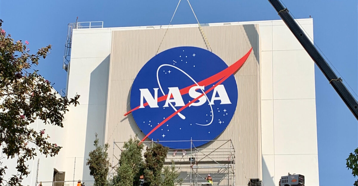 News November 17 2020 NASA s Jet Propulsion Laboratory Has a Bold New Look The sign as seen from a distance on JPL S Spacecraft Assembly Facility The sign is a vinyl covering stretched over an aluminum frame Credit NASA JPL-Caltech Larger view A giant version of NASA s classic red white and blue logo now proudly adorns a building that has played a central role in space-exploration history A new 30-foot NASA logo has been installed on the side of the Spacecraft Assembly Facility at the Jet Propulsion Lab to welcome JPLers and visitors alike The red white and blue insignia - designed in 1959 and nicknamed the meatball - went up on Oct 17 and can be spotted from the freeway nearby We have two strands of DNA - one NASA and one Caltech We wanted to proudly show our NASA heritage with this logo said JPL Director Michael Watkins With the appearance of the new sign I think that more than a few people will be surprised to realize there s a NASA center tucked away right here in the foothills of the San Gabriel Mountains NASA Video 1 52 A giant version of NASA s classic red white and blue logo now proudly adorns a building that has played a central role in space-exploration history Credit NASA-JPL Caltech Weighing 6 5 tons the logo is a vinyl covering stretched over an aluminum frame then fastened to a steel structural ring It was assembled in a parking lot at JPL before being hoisted via a 50-ton crane and fastened onto the side of the High Bay of the Spacecraft Assembly Facility the robot factory where NASA s twin Voyager spacecraft Galileo and all of the agency s Mars rovers were built Structural steel beams were welded in place to support the new sign The job of creating sizing and placing the sign fell to The Studio part of JPL s graphic design and visual strategy team The historic location they chose for the sign was only fitting although the decision was grounded in pragmatism Get the Latest JPL News Subscribe to the Newsletter We were trying to find a building that worked both in location and was the right size height and shape said Dan Goods manager of The Studio While we were originally just looking for a proper surface the fact that it s our High Bay was a happy accident that gives it more significance JPL s location at the base of the foothills dates back to 1936 when a group of rocket enthusiasts working under Caltech graduate student Frank Malina conducted rocket-firing tests at the site JPL a division of Caltech grew throughout the 1940s and 50s and ultimately built and helped launch America s first satellite Explorer 1 in 1958 By the end of that year Congress established NASA and JPL became a part of the agency Caltech manages JPL for NASA