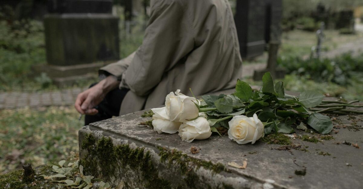 A person sitting by a tombstone with white roses evoking themes of grief and remembrance