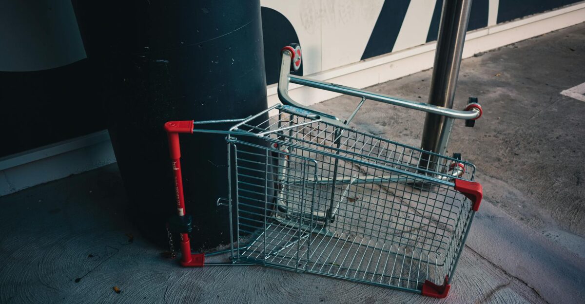 A metal shopping cart lies upside down against a building wall outdoors indicating neglect or vandalism