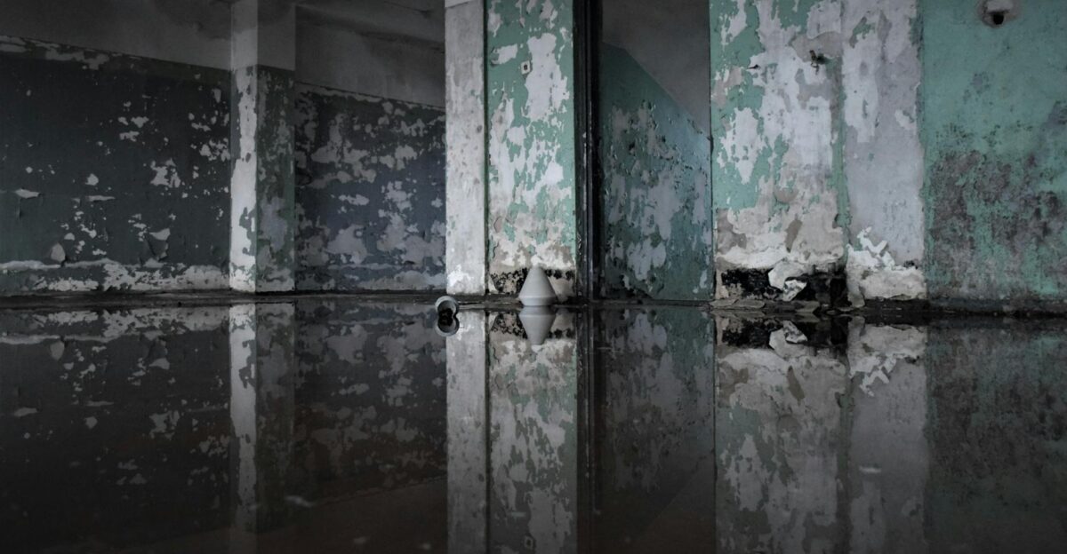 A decaying abandoned room with peeling paint and flooded floor creating a reflection effect