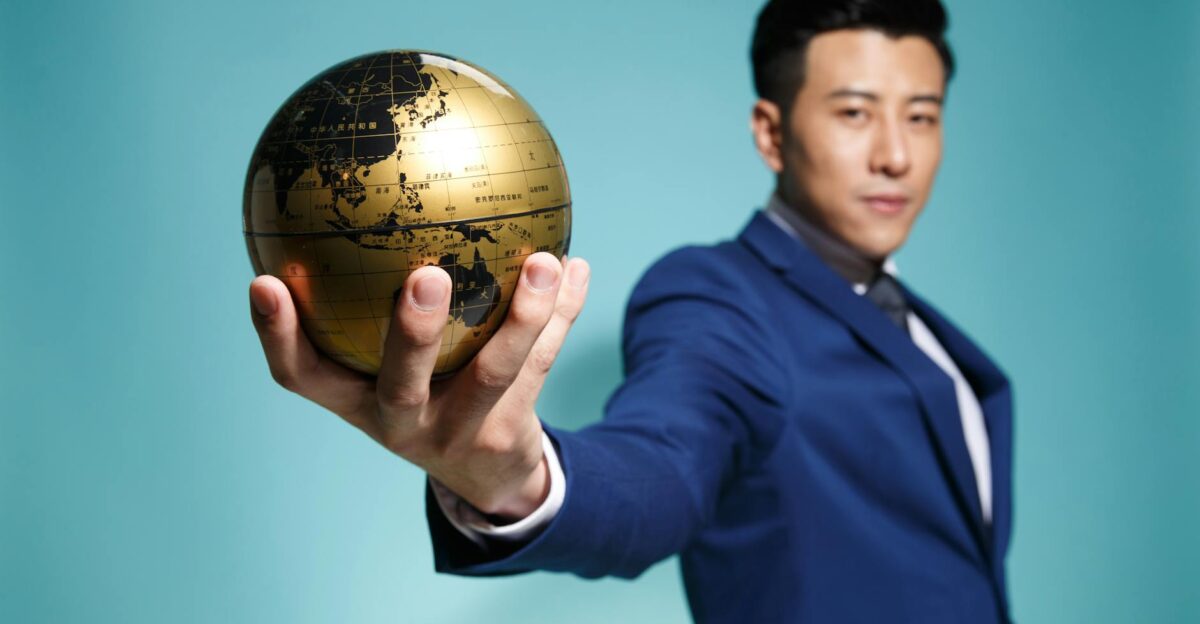 Asian businessman in blue suit confidently holding a golden globe against a blue background