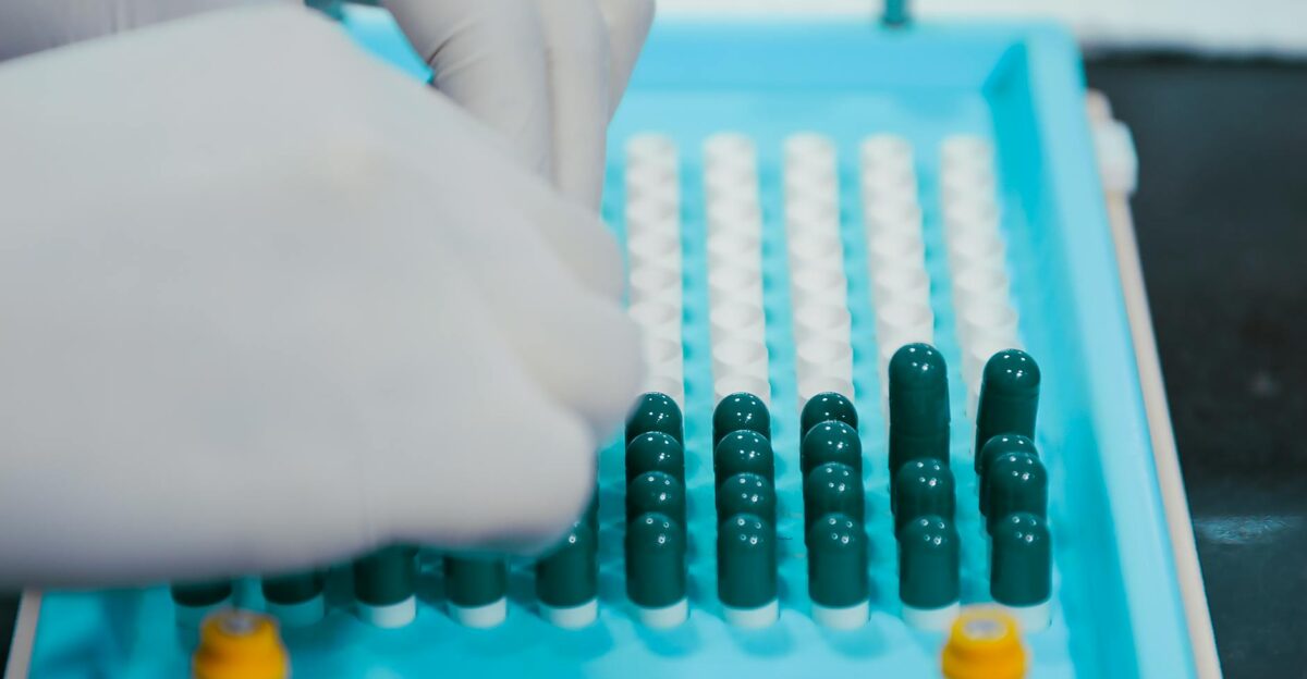 Close-up view of gloved hands arranging capsules on a sterile tray indicative of pharmaceutical practices