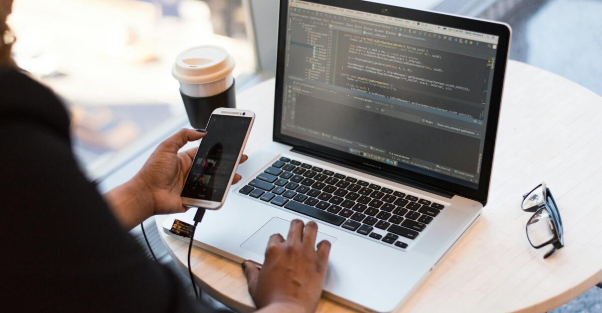 Developer working remotely coding on a laptop with phone in hand showcasing modern work culture