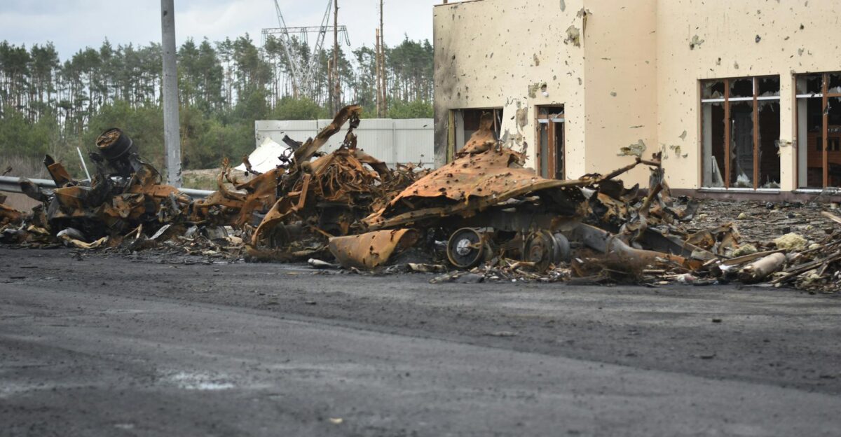 A dramatic scene depicting the aftermath of destruction with burnt vehicles and damaged building exterior
