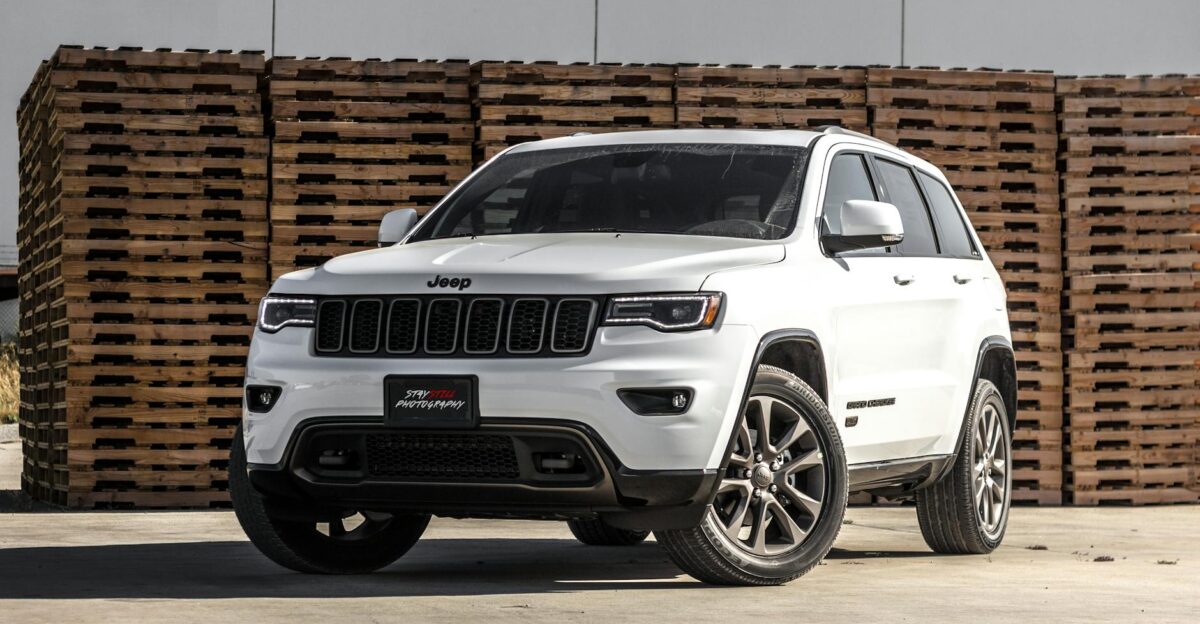 A sleek white Jeep Grand Cherokee parked in front of stacked wooden pallets showcasing its luxury features