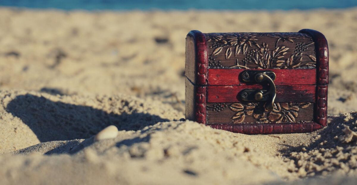 A decorative treasure chest sits on a sunny beach invoking mystery and adventure