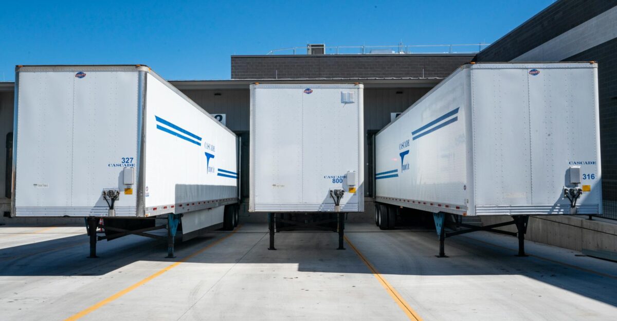 Three white cargo trailers parked at an industrial shipping dock under clear blue skies