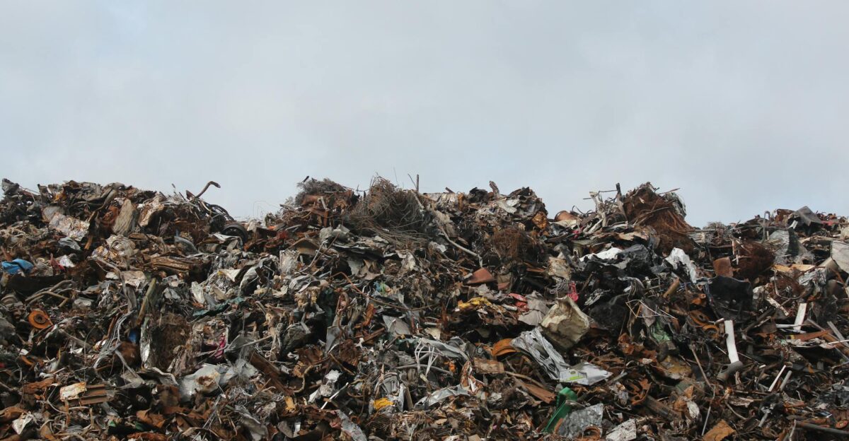 A large pile of scrap metal and waste at a landfill against a cloudy sky
