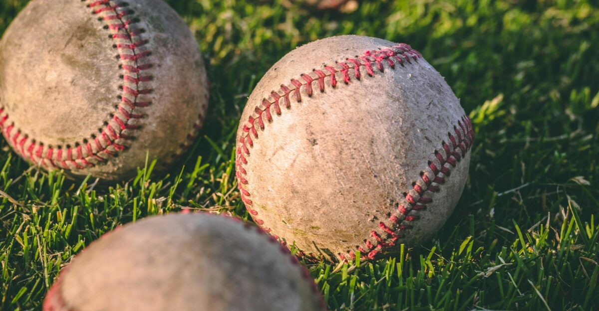 Close-up of multiple baseballs lying on a grassy field in bright sunlight