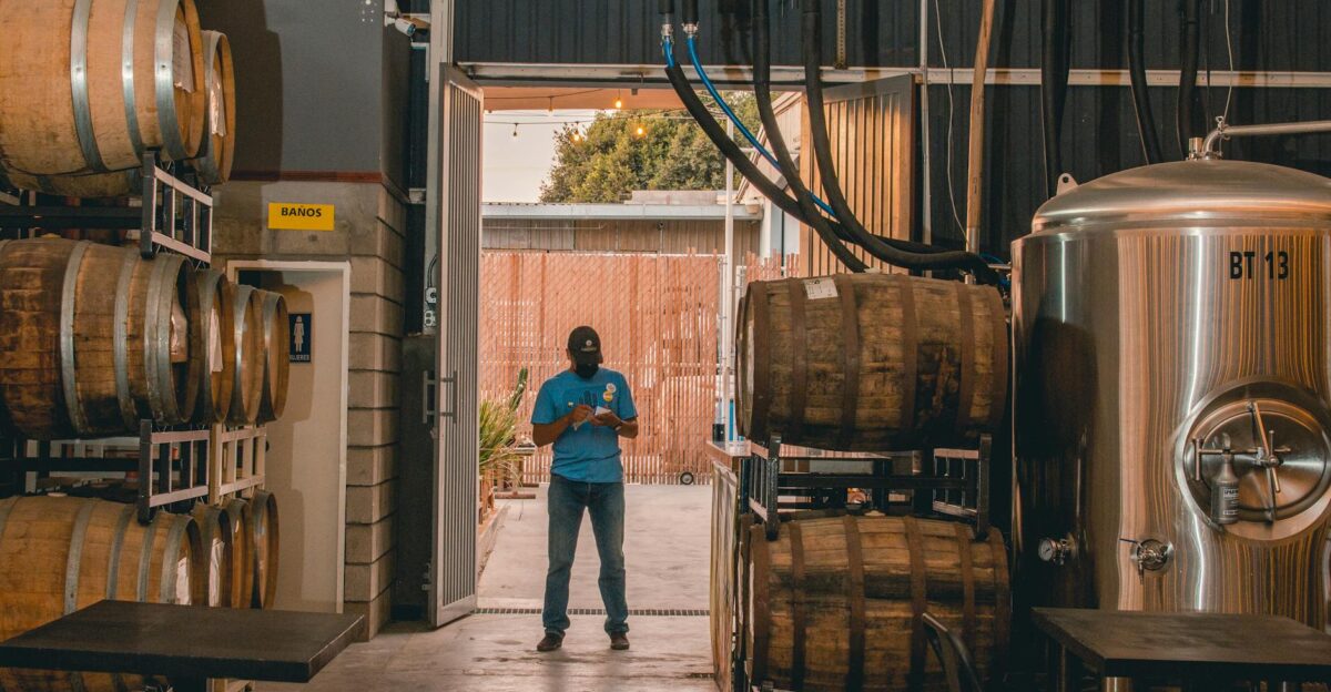 A worker stands in a brewery warehouse surrounded by kegs and equipment creating an urban industrial scene