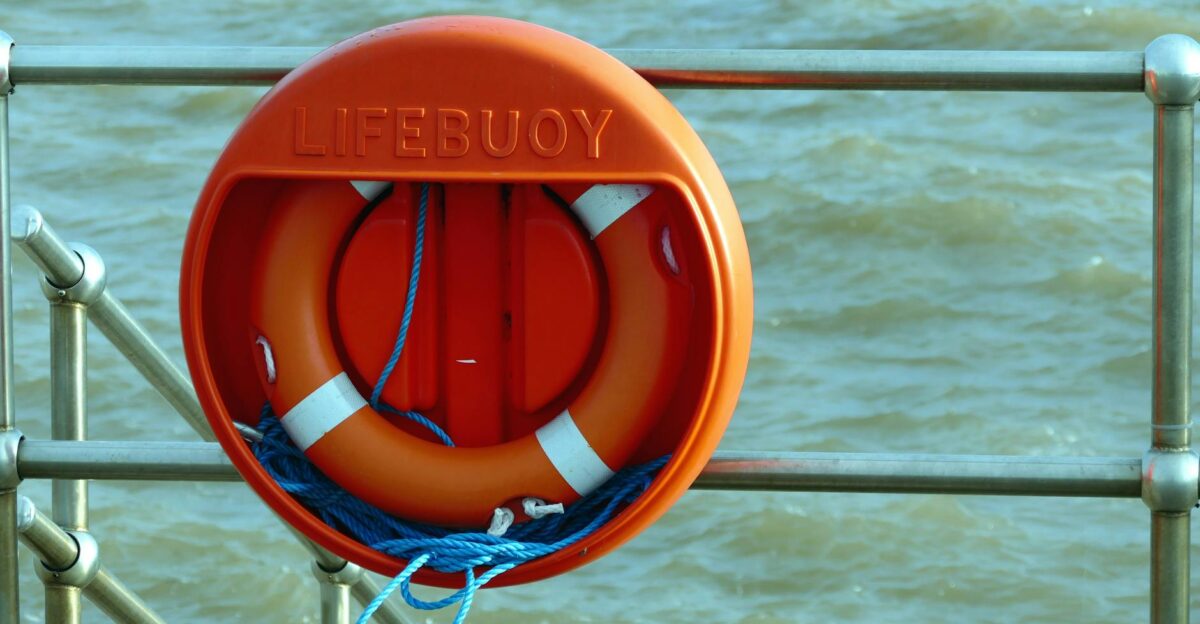 A bright orange lifebuoy hangs on a metal railing overlooking the sea signifying safety at the coast
