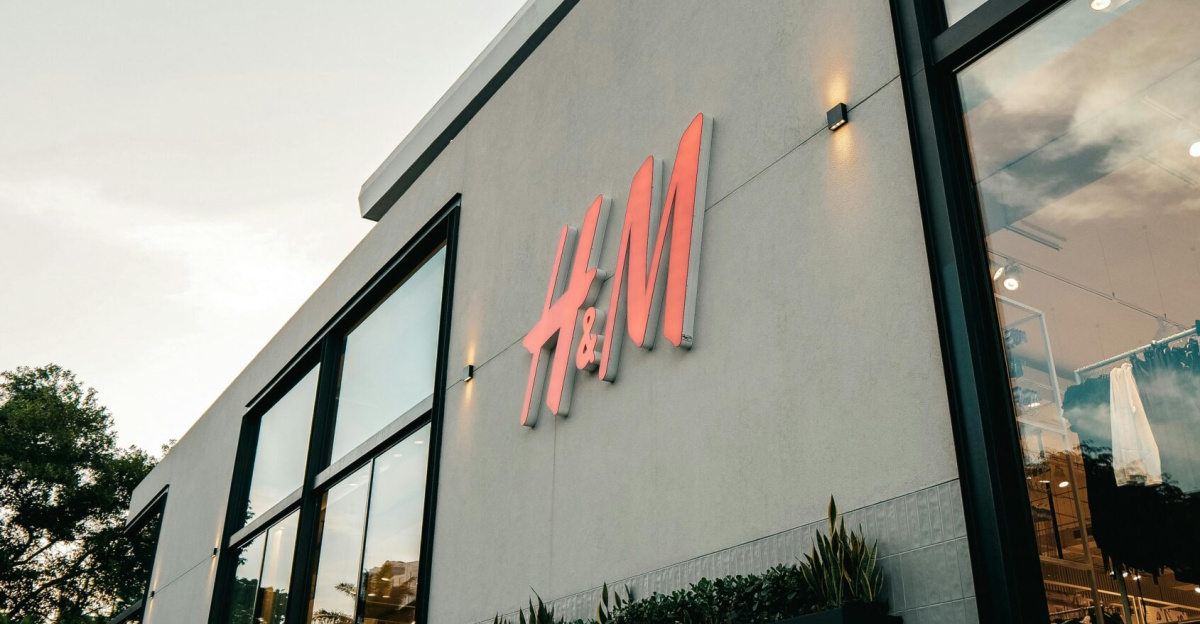 Low angle shot of a modern H&M store exterior featuring green grass and clear sky.