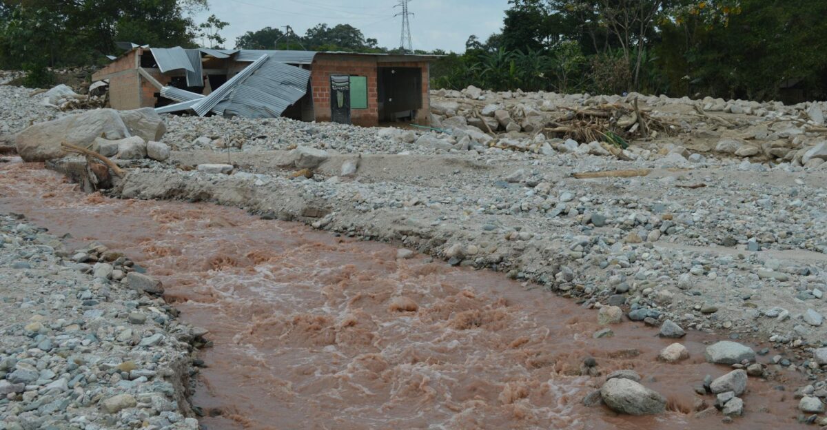 A damaged house stands near a muddy river after a flood illustrating the impact of natural disasters