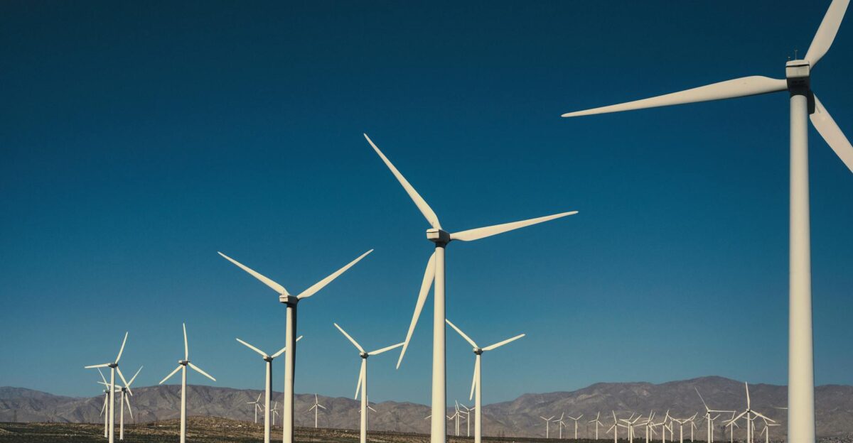A vast landscape of wind turbines generating clean energy with a backdrop of mountains and a clear blue sky