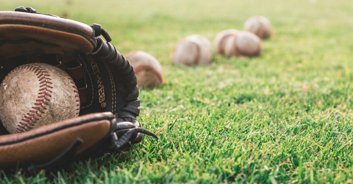 A close-up of a baseball glove with balls on a green field symbolizing outdoor sports