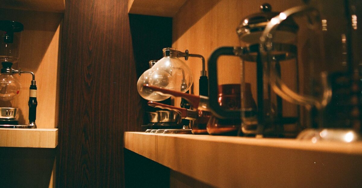 Warm indoors scene of a wooden shelf with various coffee makers and accessories