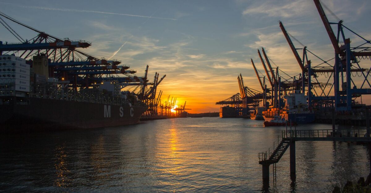 Shipping vessels at Hamburg port during a vibrant sunset showcasing industrial cranes