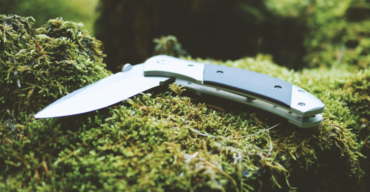 Folding knife resting on a lush moss-covered surface in a forest. Ideal for camping gear and outdoor enthusiasts.