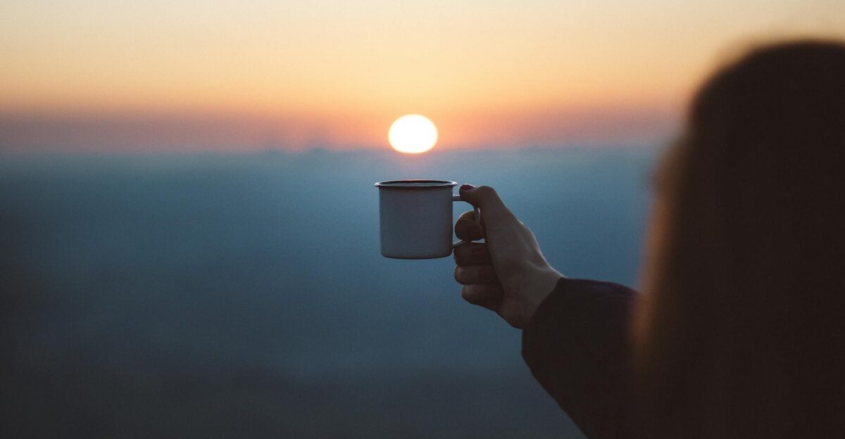A person holds a coffee cup against a beautiful sunrise capturing a serene outdoor moment