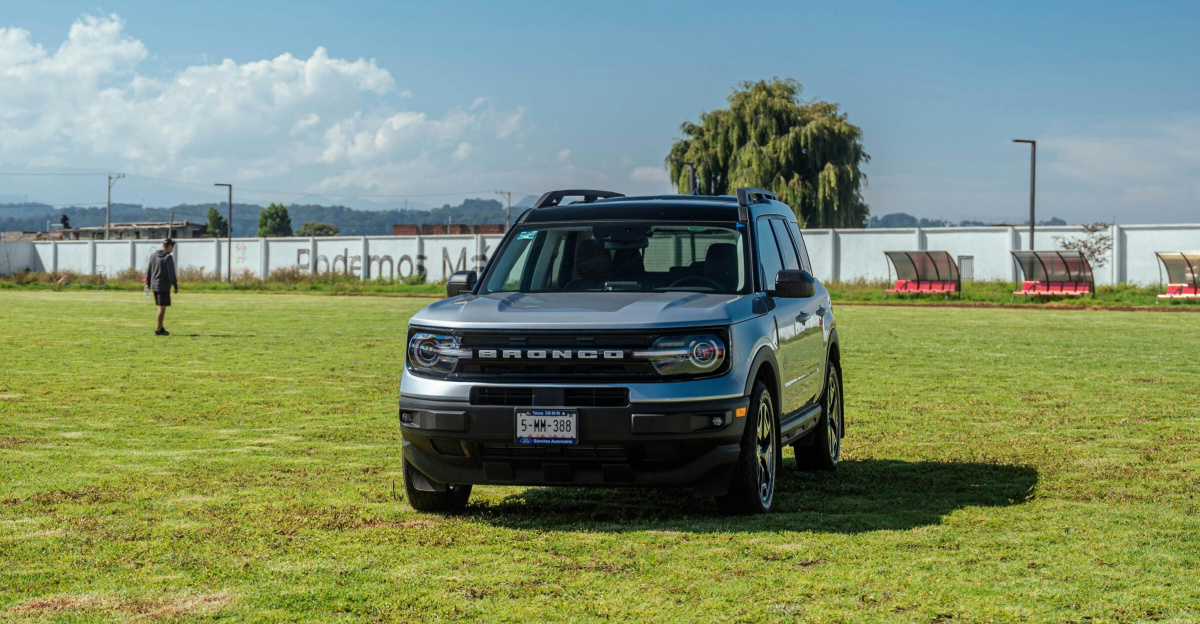 A silver Ford Bronco park on a grassy field under a blue sky, showcasing a rural landscape.