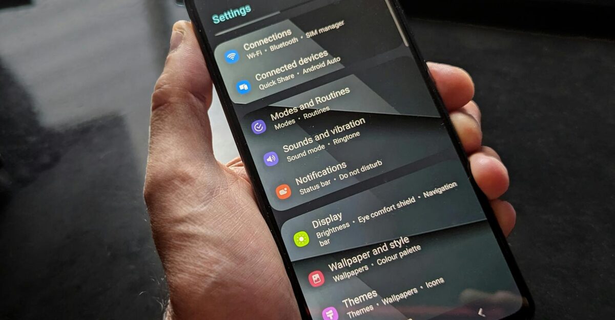 Hand holding smartphone displaying settings screen with various options evident