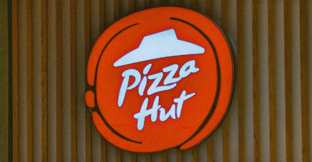 Illuminated Pizza Hut sign on a wooden storefront captured in daylight.