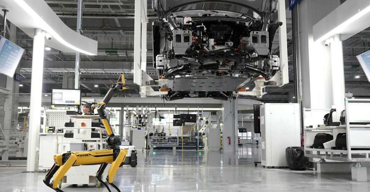 A robotic dog oversees an automated car assembly in a high-tech factory setting