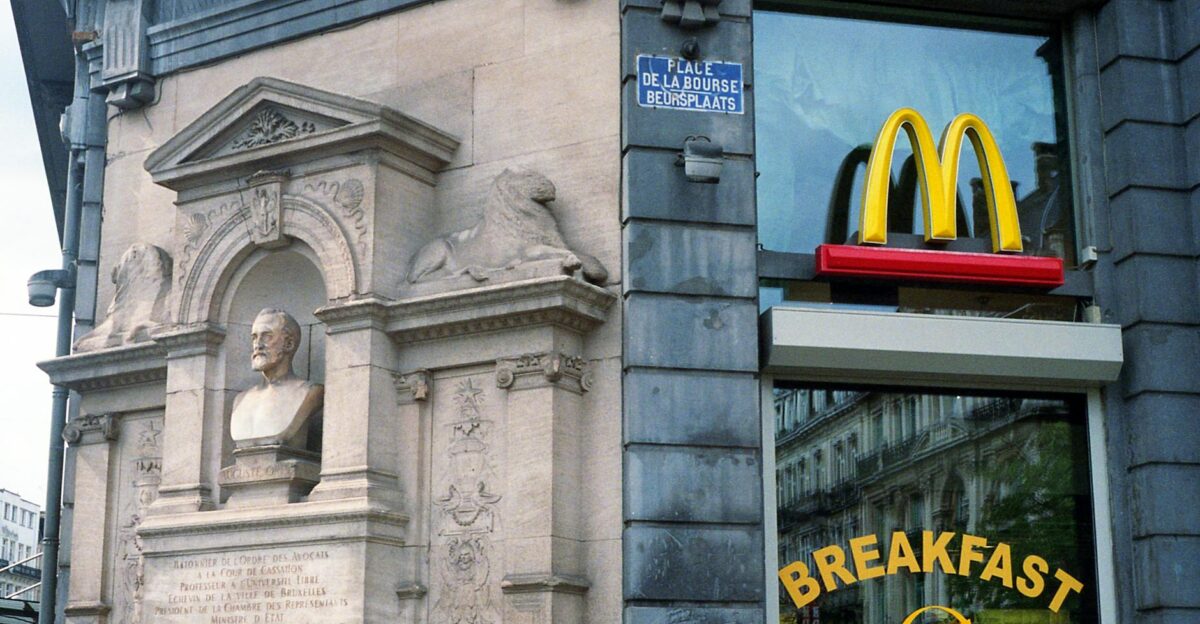 A historic building corner in Brussels featuring a McDonald s sign and a classical sculpture