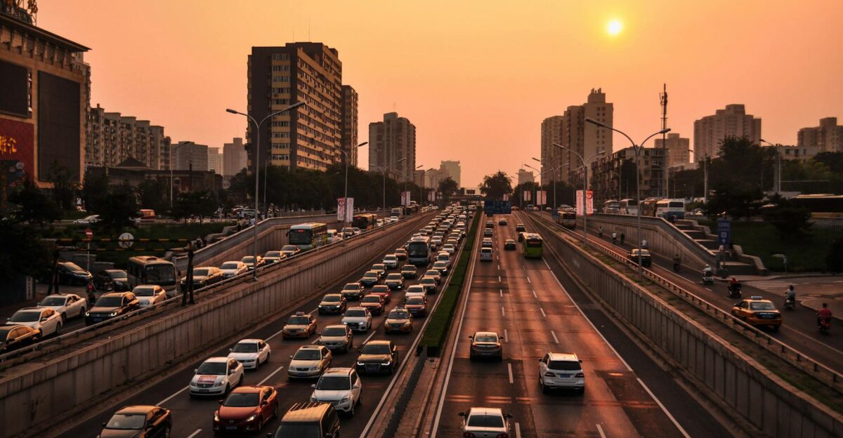 A bustling urban highway with heavy traffic under a vibrant sunset sky against a cityscape backdrop