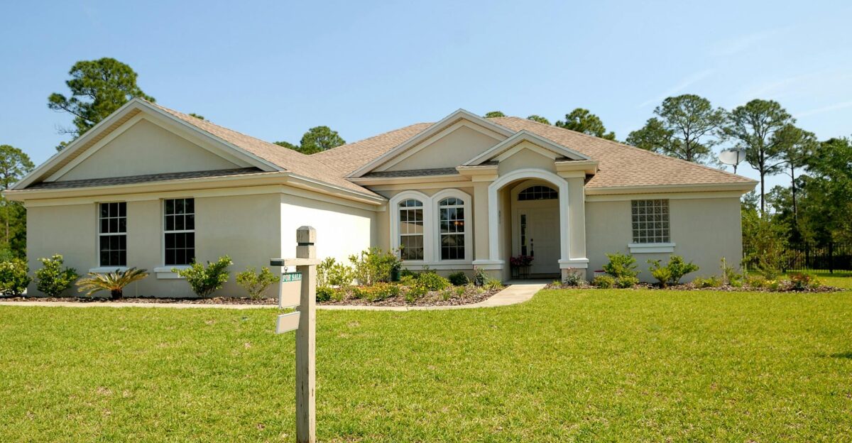 Beautiful suburban house with lush lawn showcasing a for sale sign under a clear blue sky