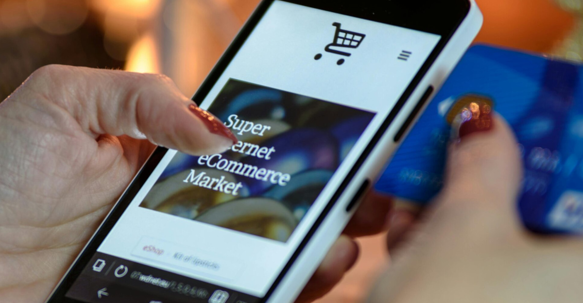 Woman using smartphone for online shopping with credit card in hand, festive background lighting.