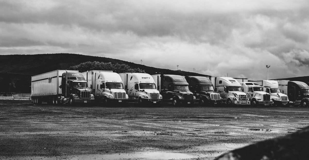 Row of parked semi trucks in a rainy lot captured in a dramatic black and white setting
