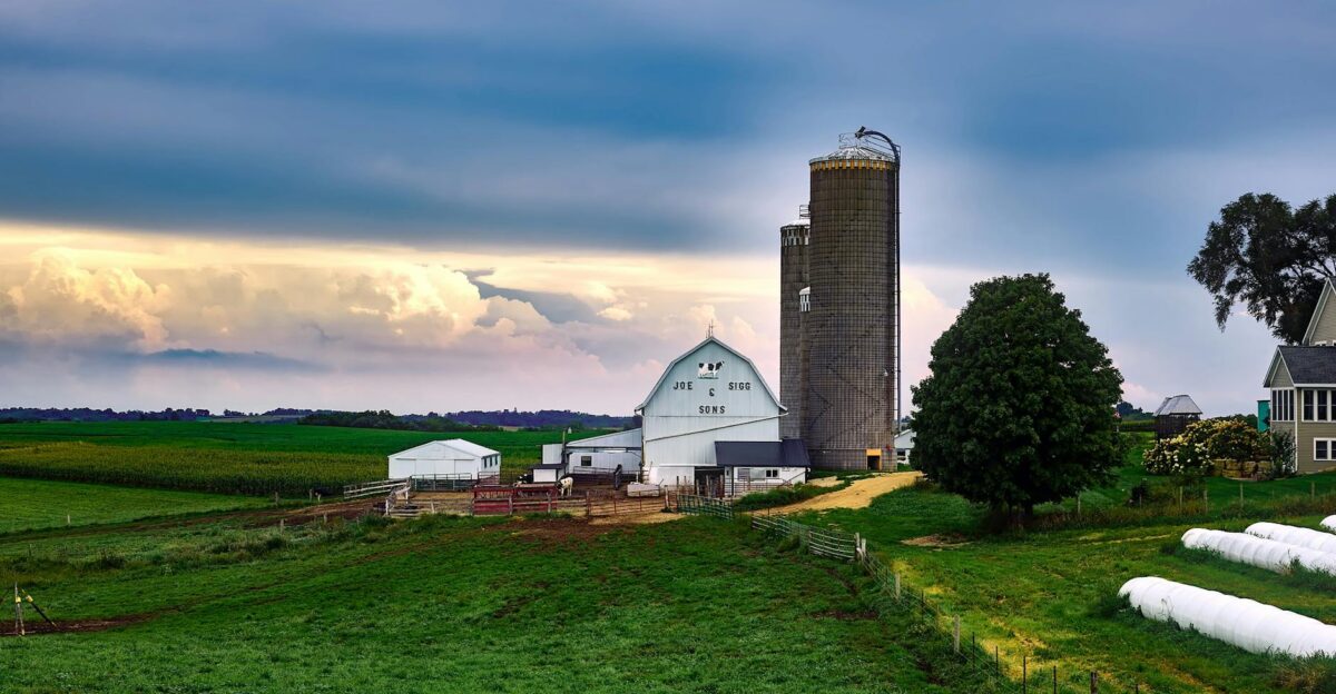 A serene view of a traditional farm with a barn and silo under dramatic sunset skies in Wisconsin countryside