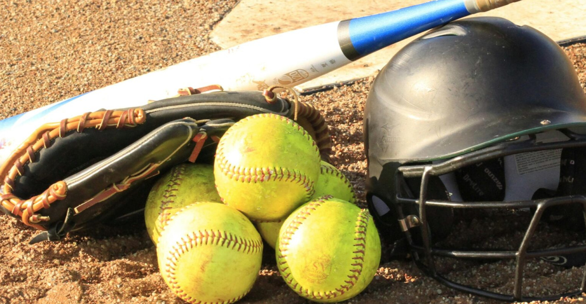 Close-up of baseball and softball gear on a dirt field, ready for a game.