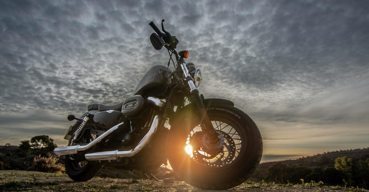 A striking image of a motorcycle parked on a dirt road with a dramatic sky at sunset capturing the sun glare