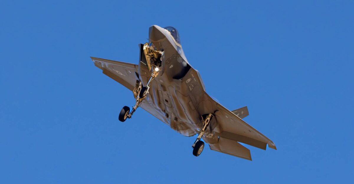 A military jet is captured flying under a bright blue sky showcasing its aerodynamic design